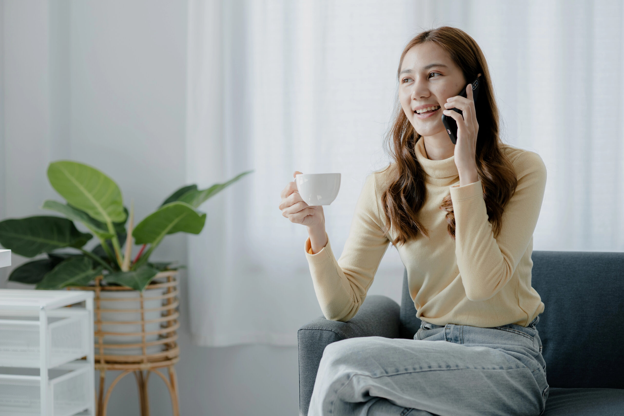 Smiling person enjoying a warm drink while talking on the phone at home